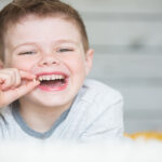 young boy smiling and holding his tooth that has just fallen out