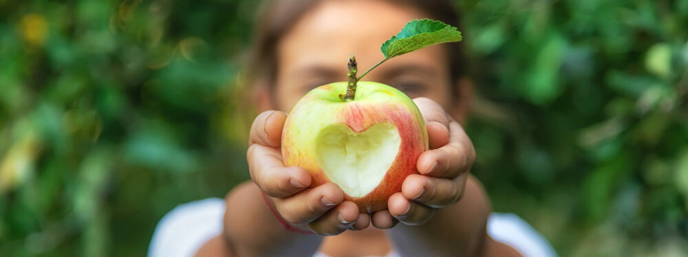 Young girl holding an apple with a heart shape cut into it.