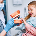 Young girl at first dental appointment playing with model of teeth with a pediatric dentist.