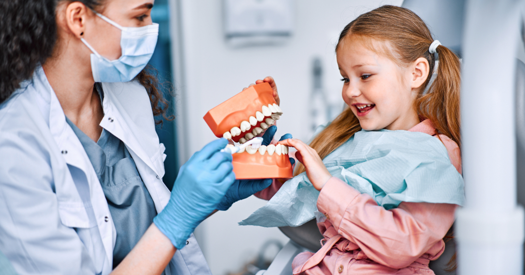 Young girl at first dental appointment playing with model of teeth with a pediatric dentist.