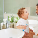 Mother teaches young child how to brush his baby teeth.