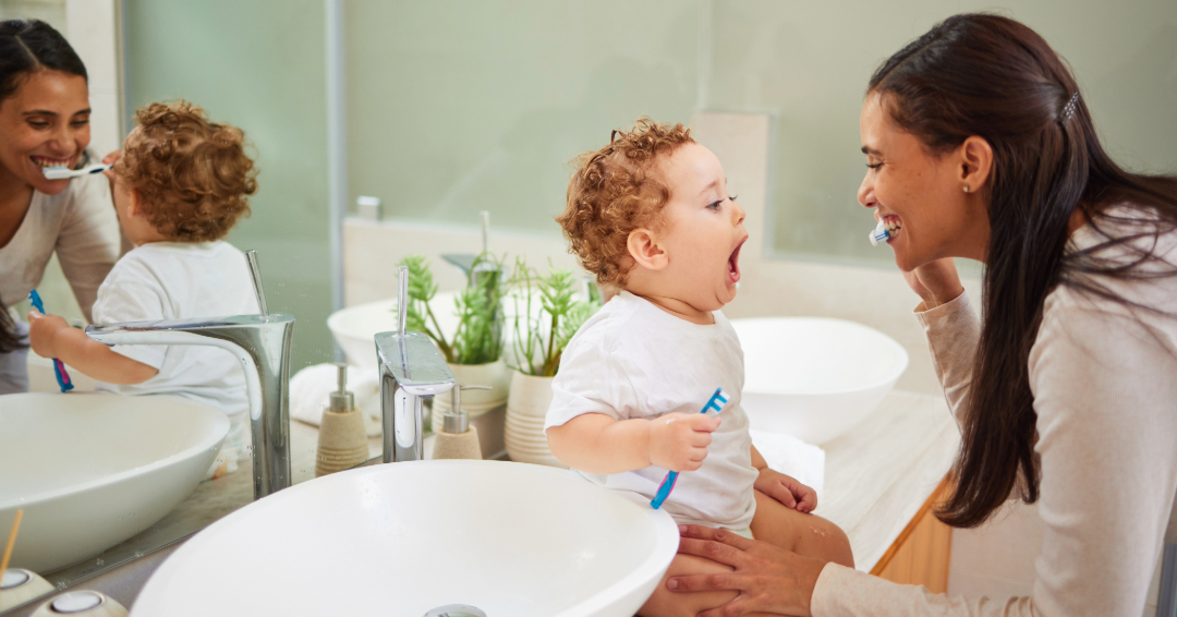 Mother teaches young child how to brush his baby teeth.