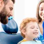 Pediatric dentist and dental assistant showing a child his smile in a tooth shaped mirror.