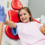 Girl in dentist’s chair high-fiving dental hygienist.