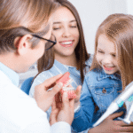 little girl sitting on her mom’s lap while talking to a dentist