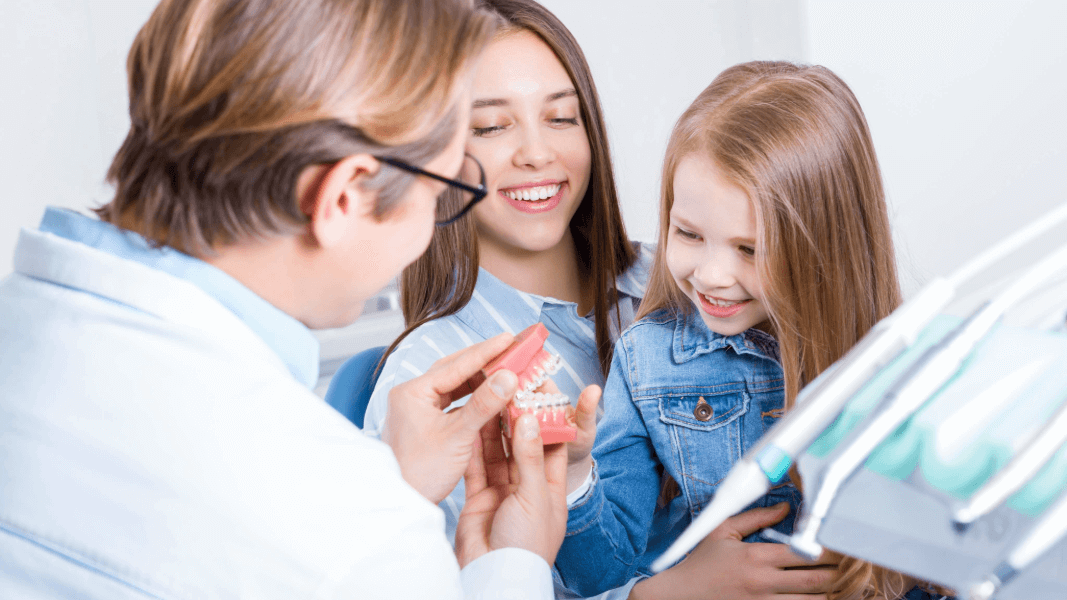 little girl sitting on her mom’s lap while talking to a dentist